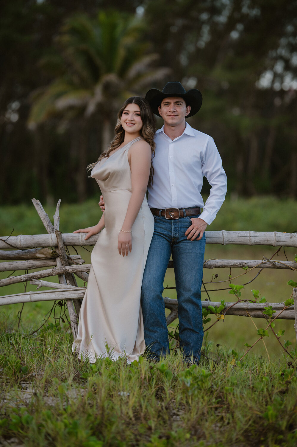 Fátima y Azael de pie junto a una cerca de madera en el campo